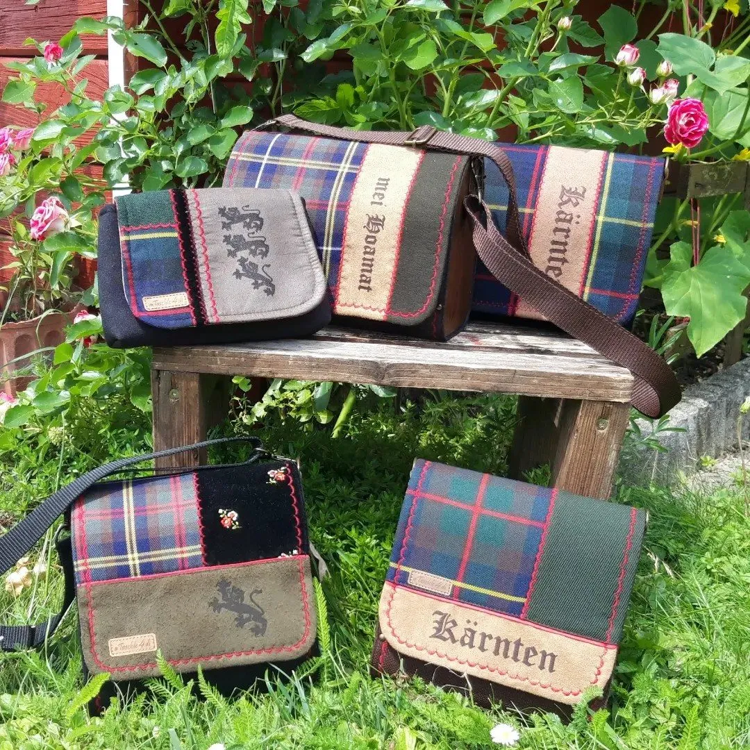 Taschen aus Karo- und Trachtenstoff mit Kärnten-Schriftzug in einem Blumengarten